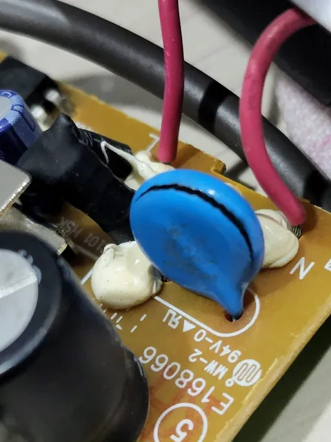 A cracked blue disc component sits among wires and capacitors on a circuit board.