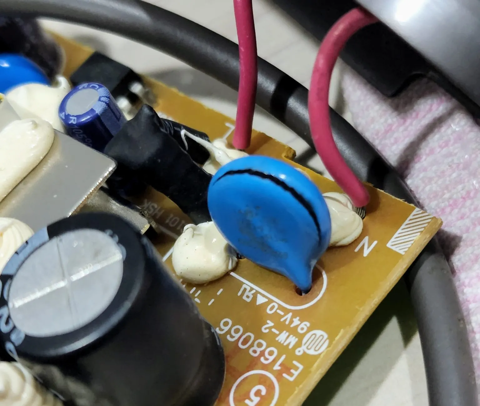 A cracked blue disc component sits among wires and capacitors on a circuit board.