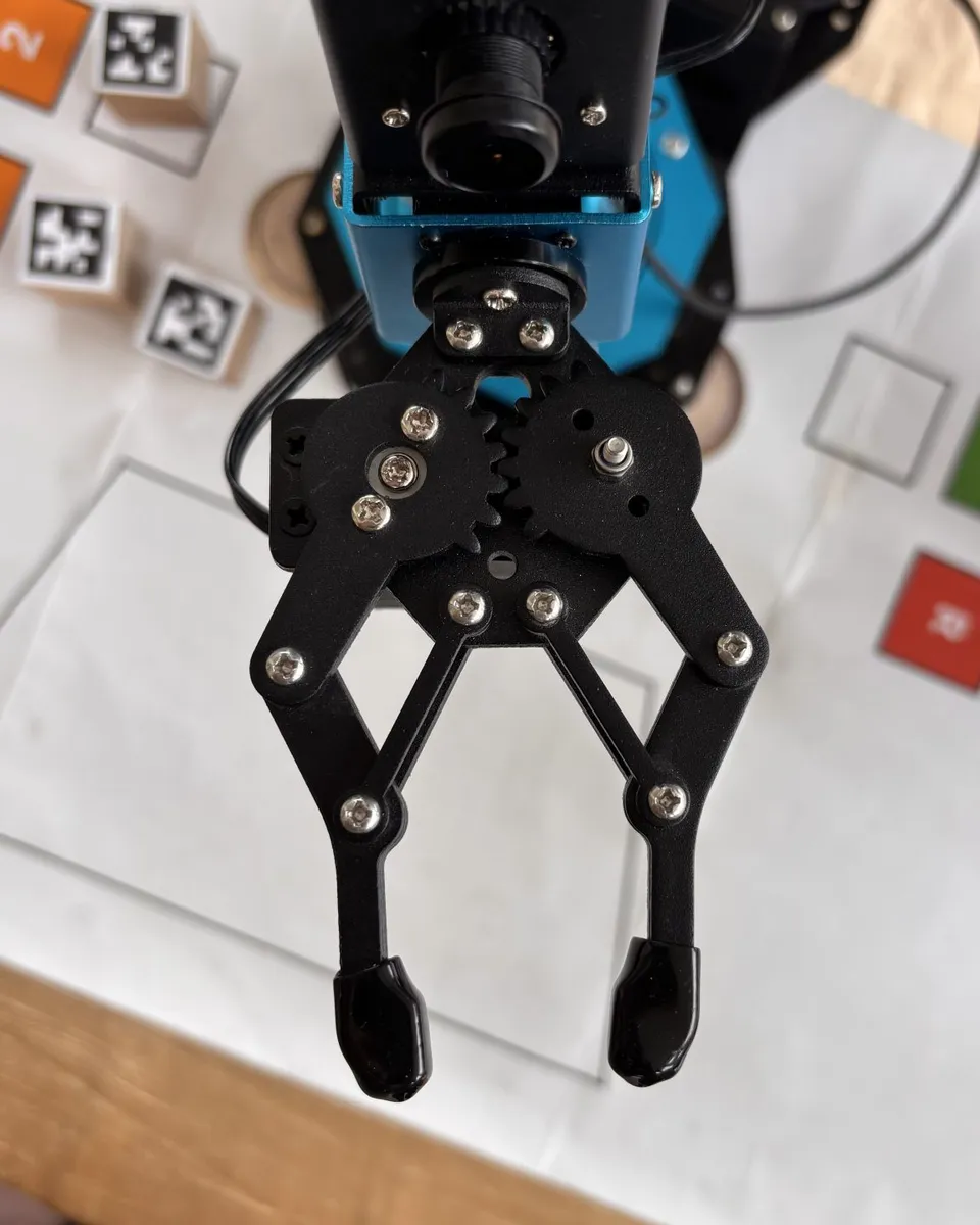 A black mechanical gripper is mounted below a small camera on a blue frame.