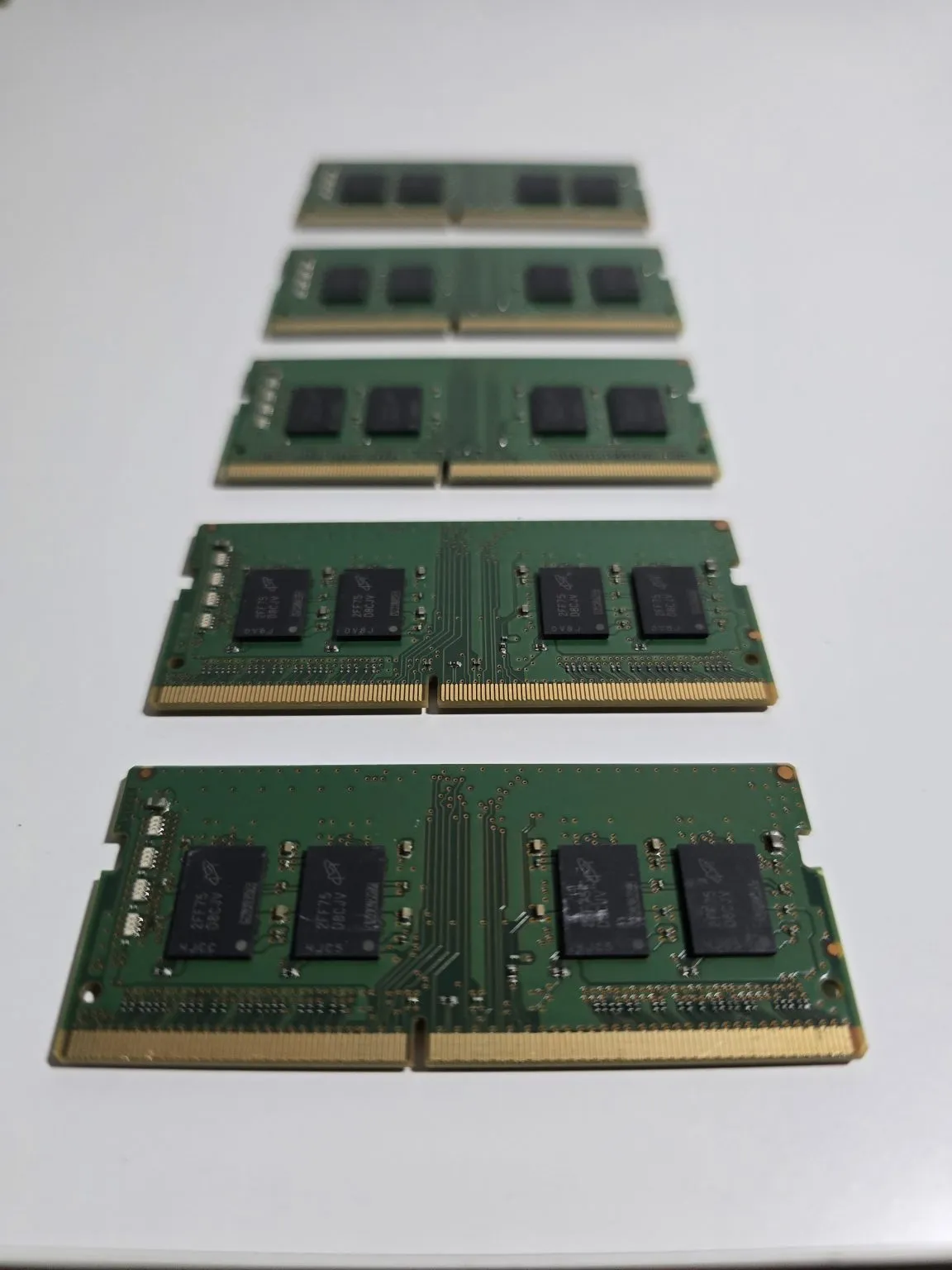 Five green laptop memory modules are arranged in a row on a pale surface.