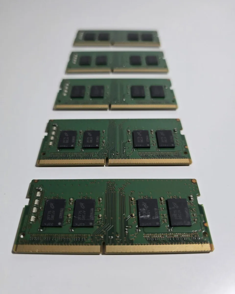 Five green laptop memory modules are arranged in a row on a pale surface.